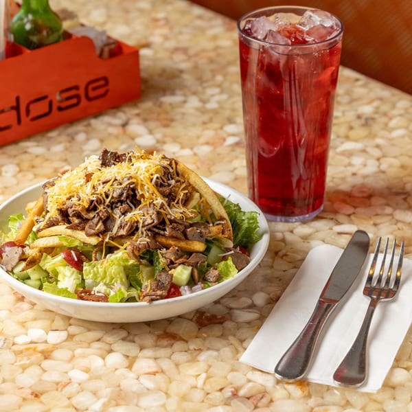 A steak salad with fries and cheese, a red drink, and cutlery on a stone table.