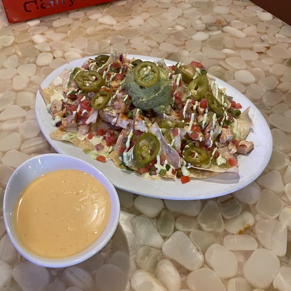Chicken nachos with guacamole, jalapeños, and pico de gallo, served with a side of cheese dip.