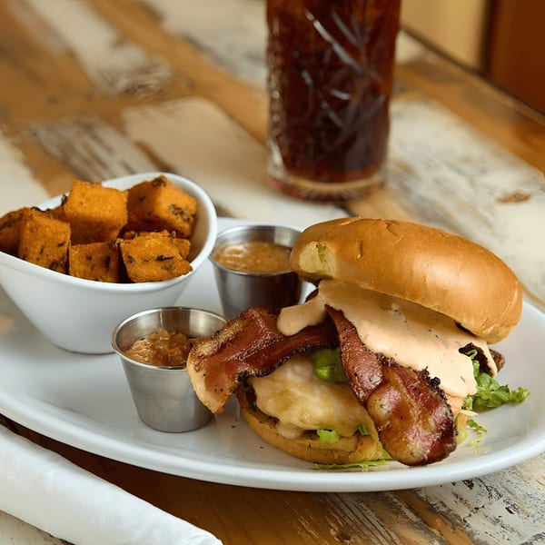 A bacon cheeseburger with a side of sweet potato fries and two dipping sauces.