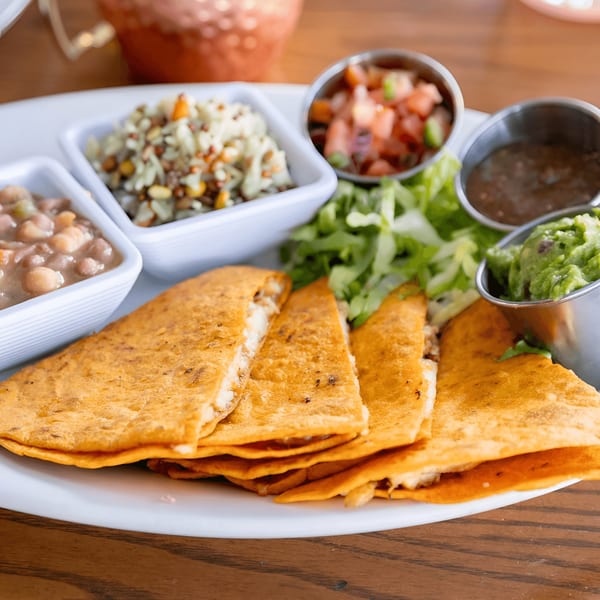 A plate of quesadillas with sides of beans, rice, salsa, guacamole, and lettuce.